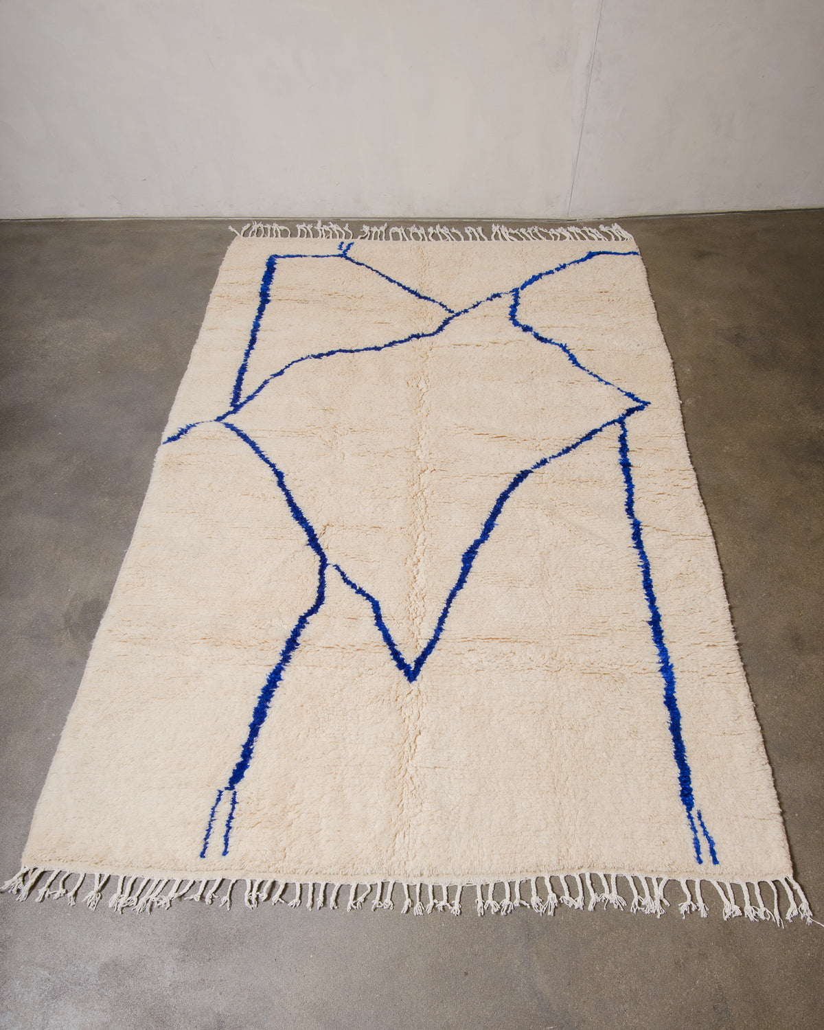 Berberlin Azilal rug made of fluffy cream wool and a minimalist blue line design, laying on cement floor.